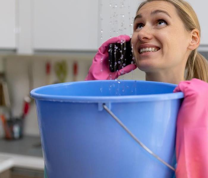 A woman holding a bucket catching water on a phone. 